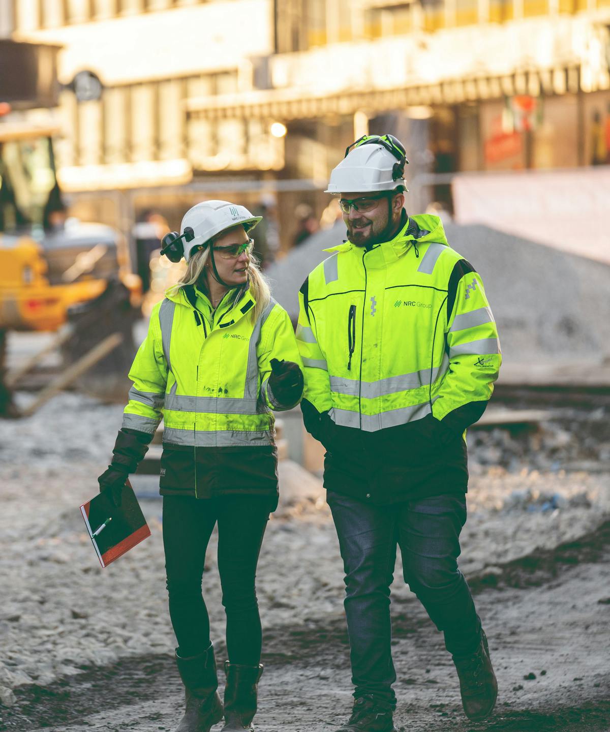 Two people walking and talking, wearing hardhats and safety glasses
